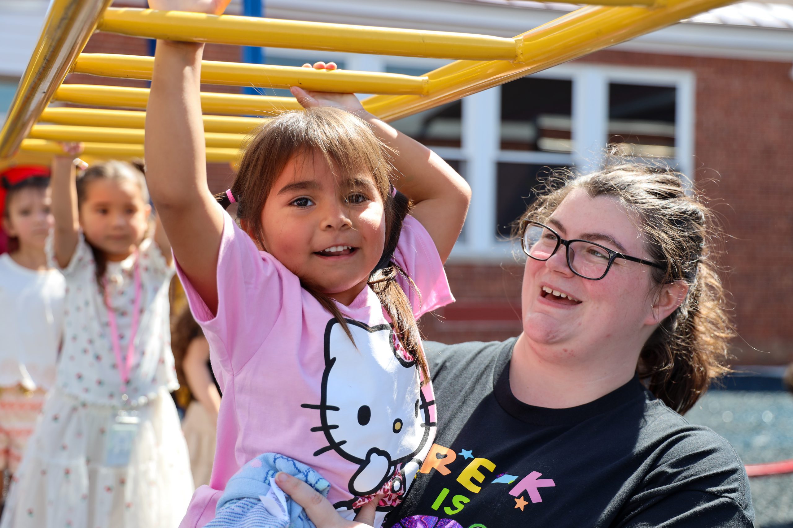 A student using monkey bars with the help of an adult