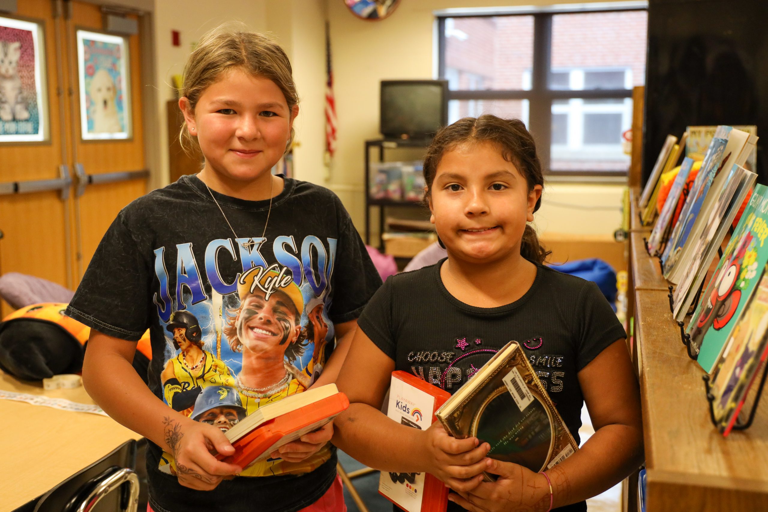 Two students holding books in a library