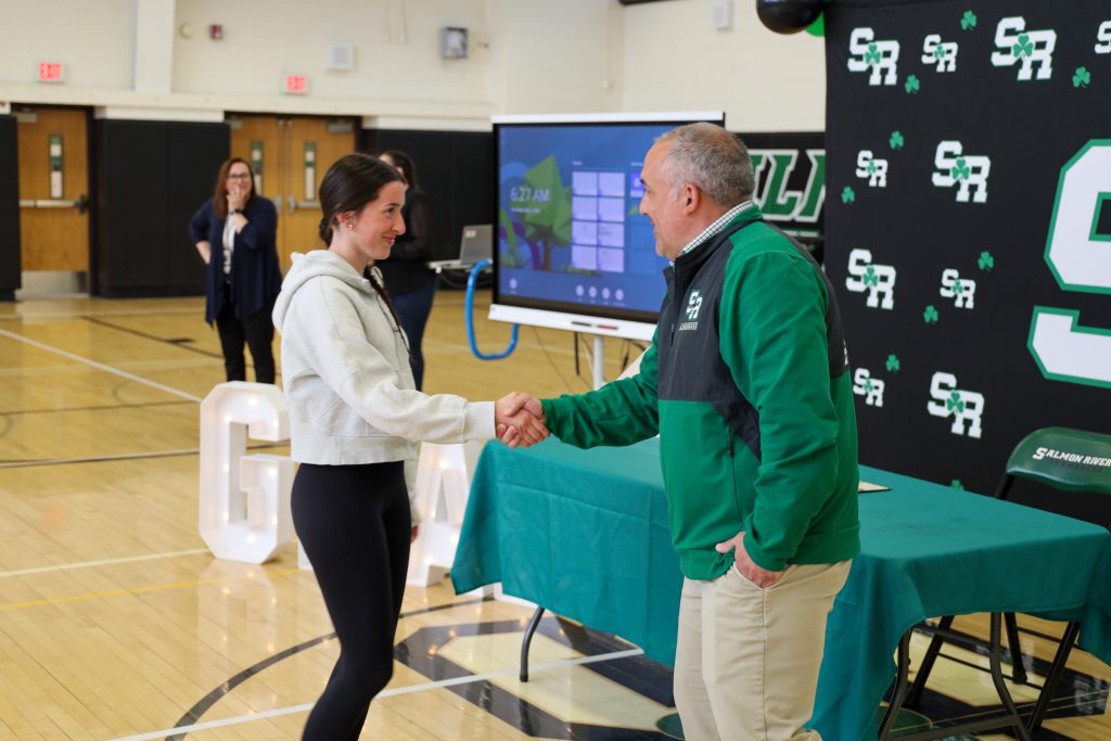 A student shaking hands with a school district employee in a gym