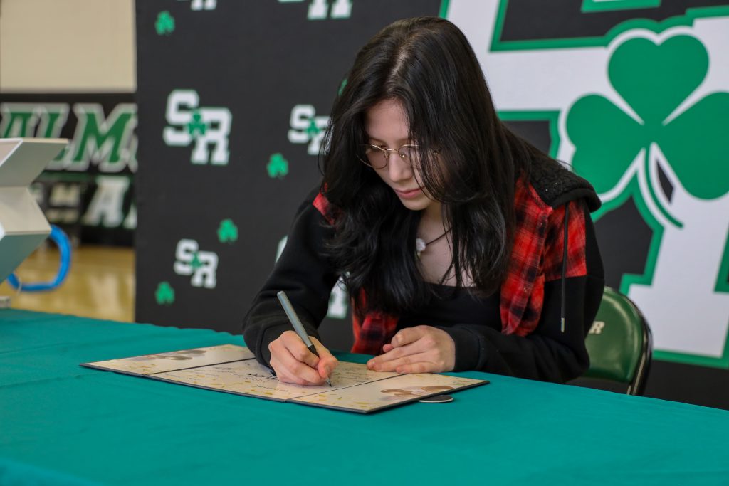 A student sitting at a table signing something into a book