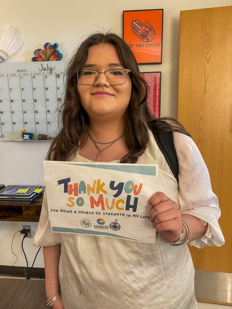 A student holding a paper that says 'Thank you so much! for being a source of strength in my life'