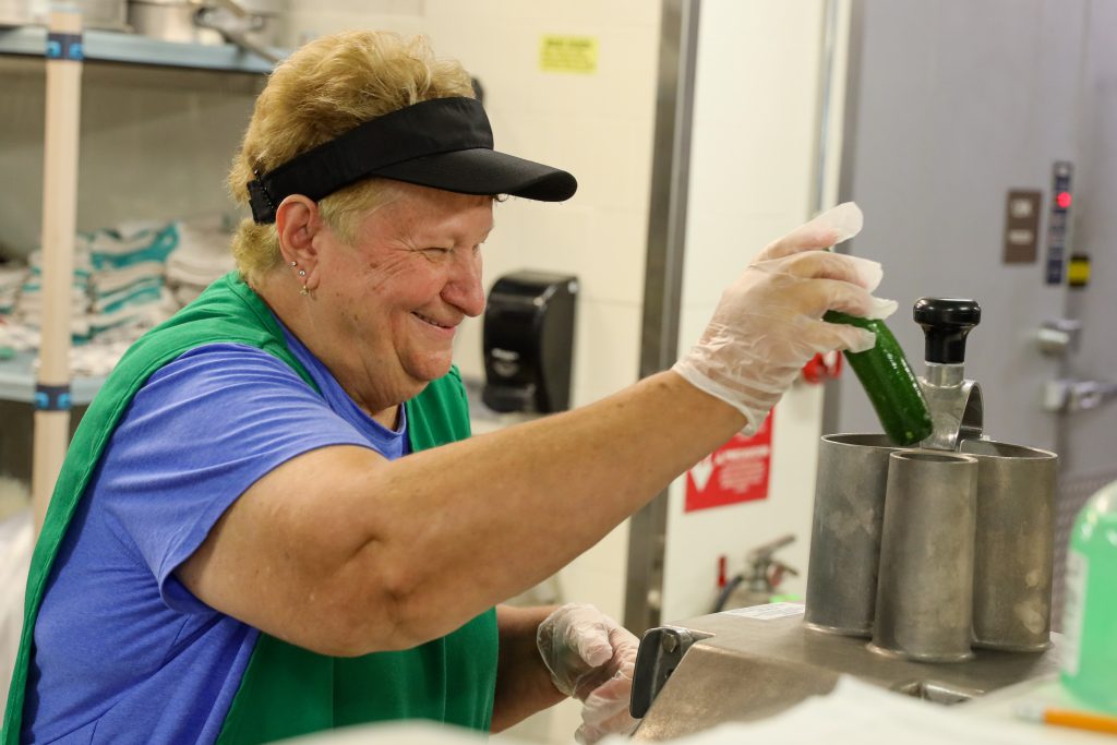 A woman wearing a vest and visor while holding a zucchini 