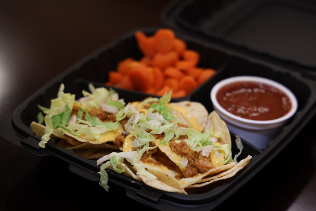 A lunch tray containing nachos, salsa and carrots