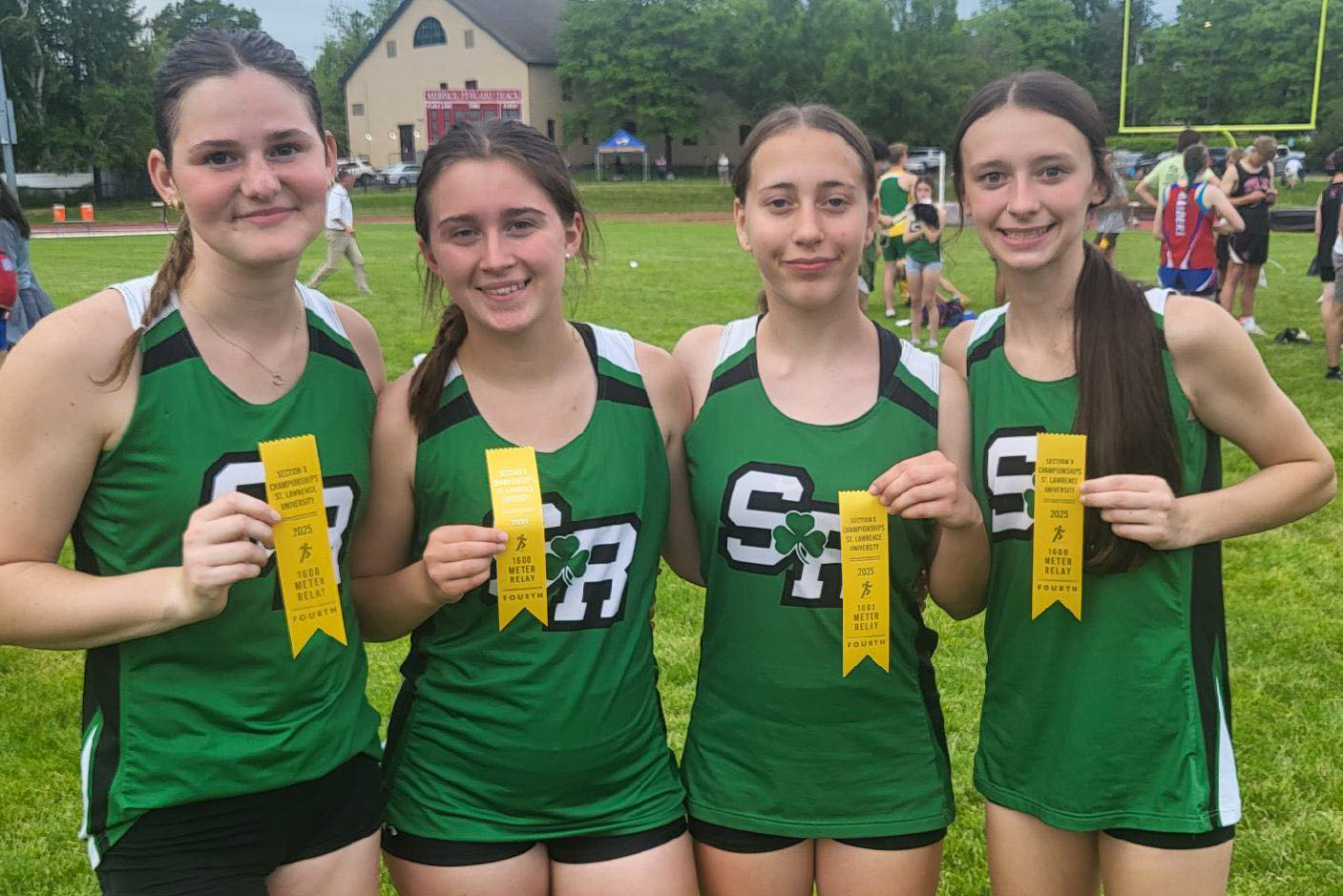 Four students wearing outdoor track uniforms holding up ribbons