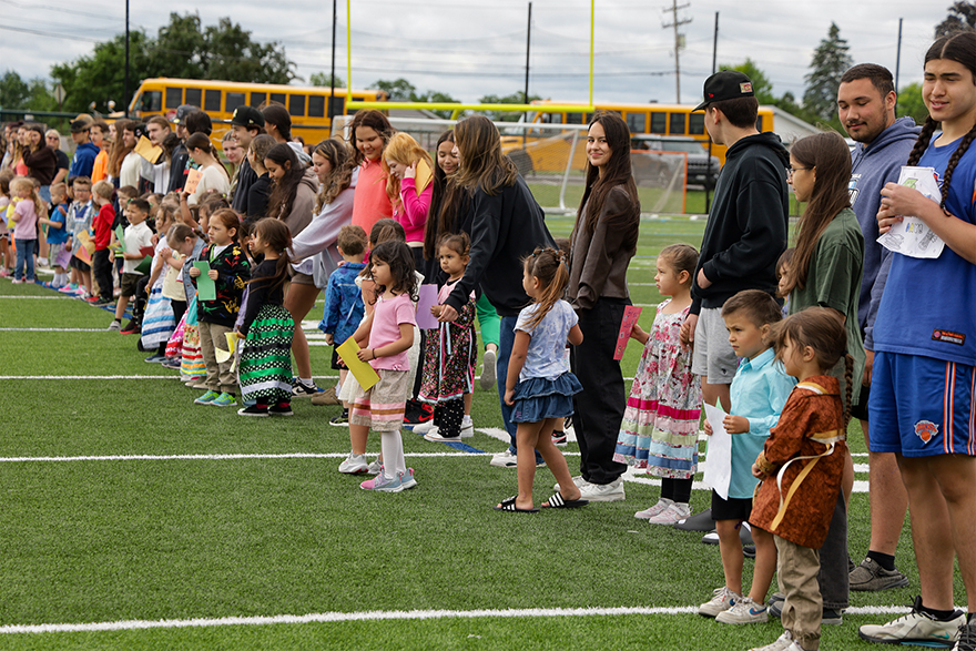Young students standing on a football field in front of older students